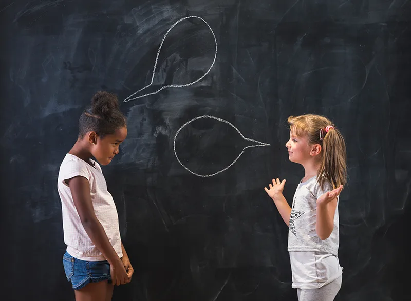 girls-speech-bubbles--AdobeStock_402429040 Girls talking in front of a chalkboard with speech bubbles